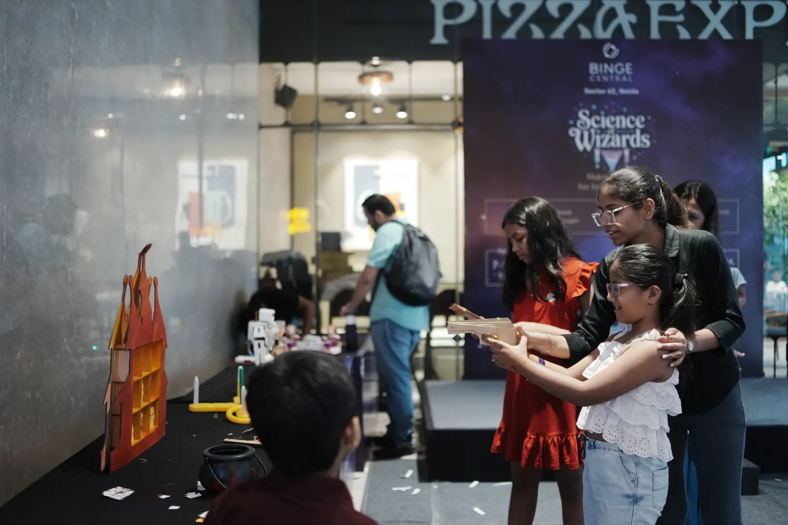 A mother steadying her daughter’s aim at a castle target game — a parent enjoying the party rather than running it