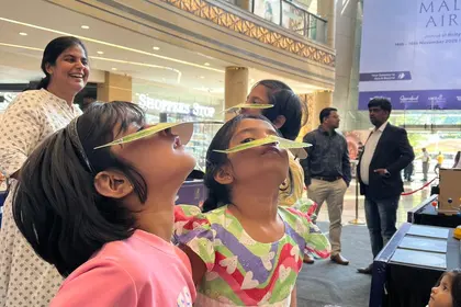 Children laughing as they balance paper birds on their noses at a mall science stand