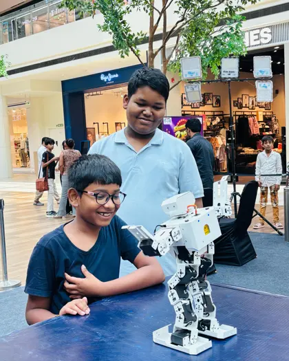 A boy grinning beside the humanoid robot he has been programming
