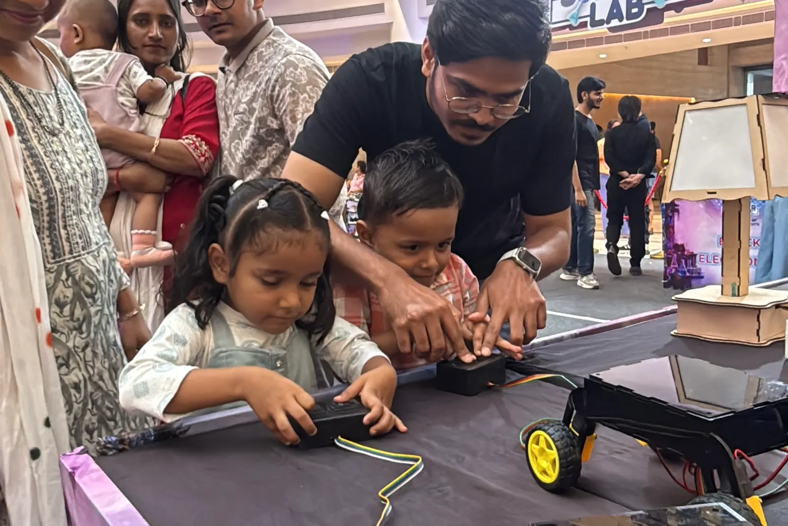 A father and two children assembling a motorised car kit at a Summer Lab table