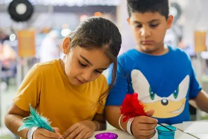Two children writing with feather quills and coloured ink