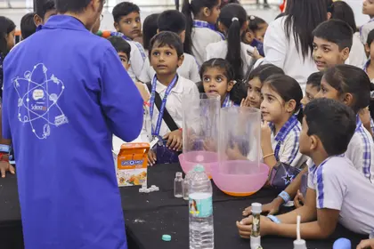 A MakerMasti science performer in a branded lab coat running a foam reaction for a ring of children