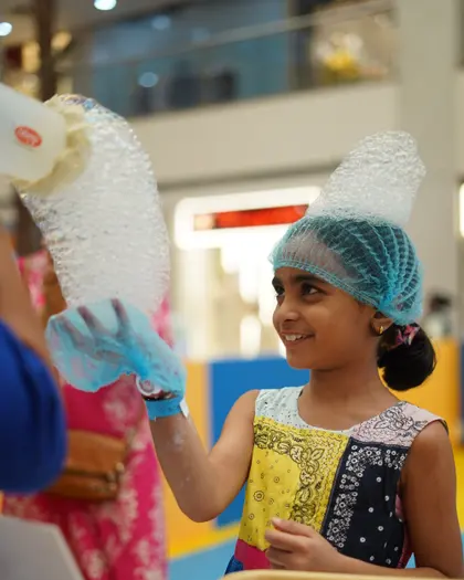 A girl in a hairnet holding up hands covered in blue reaction foam
