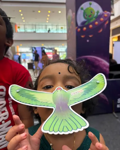 A girl holding a green paper bird glider up in front of her face