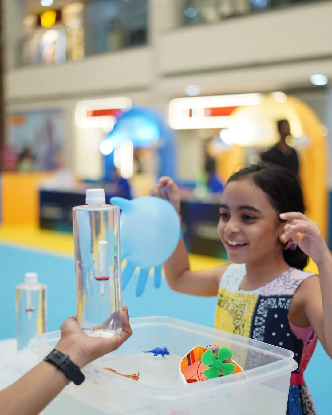 A girl watching coloured liquid climb the glass hand boiler she is holding