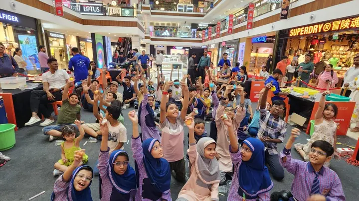 A hall full of school children with their hands in the air during a MakerMasti science show