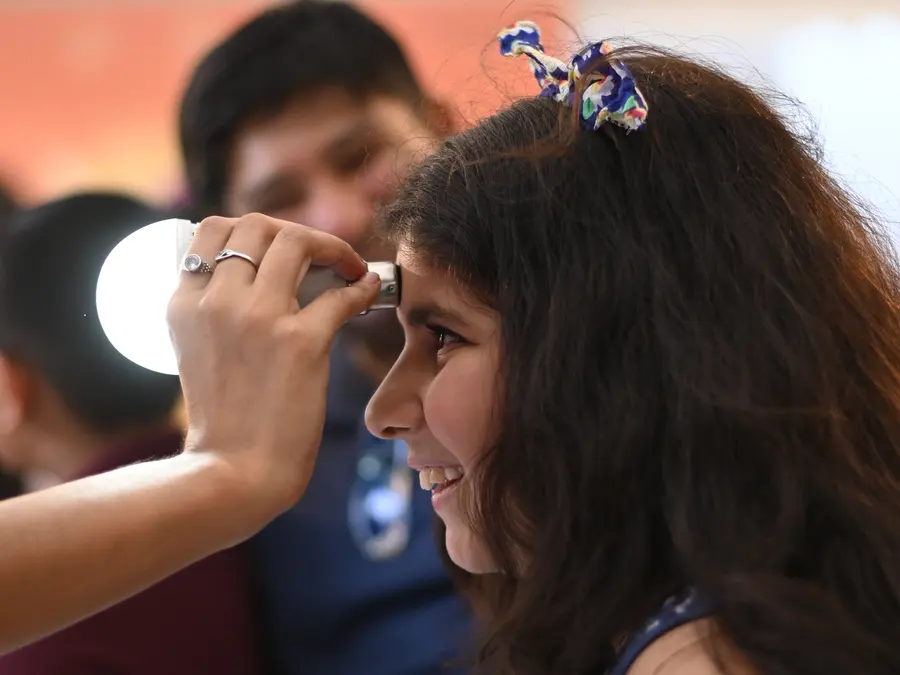 A girl laughing as a MakerMasti host holds a bright lamp to her forehead during a light experiment
