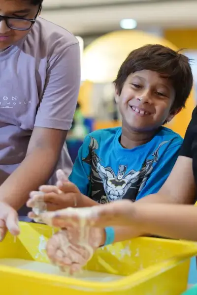 Two children laughing with their hands buried in a tray of bright yellow slime