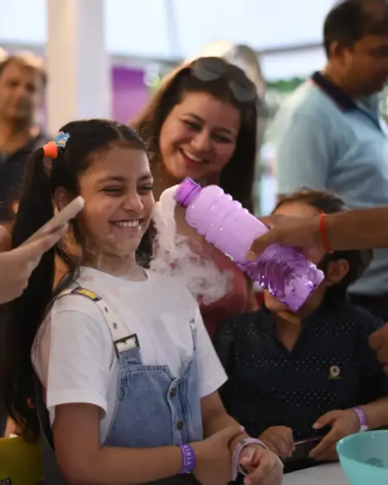 A girl grinning as a MakerMasti host pours a foaming potion over her hands at a science birthday party